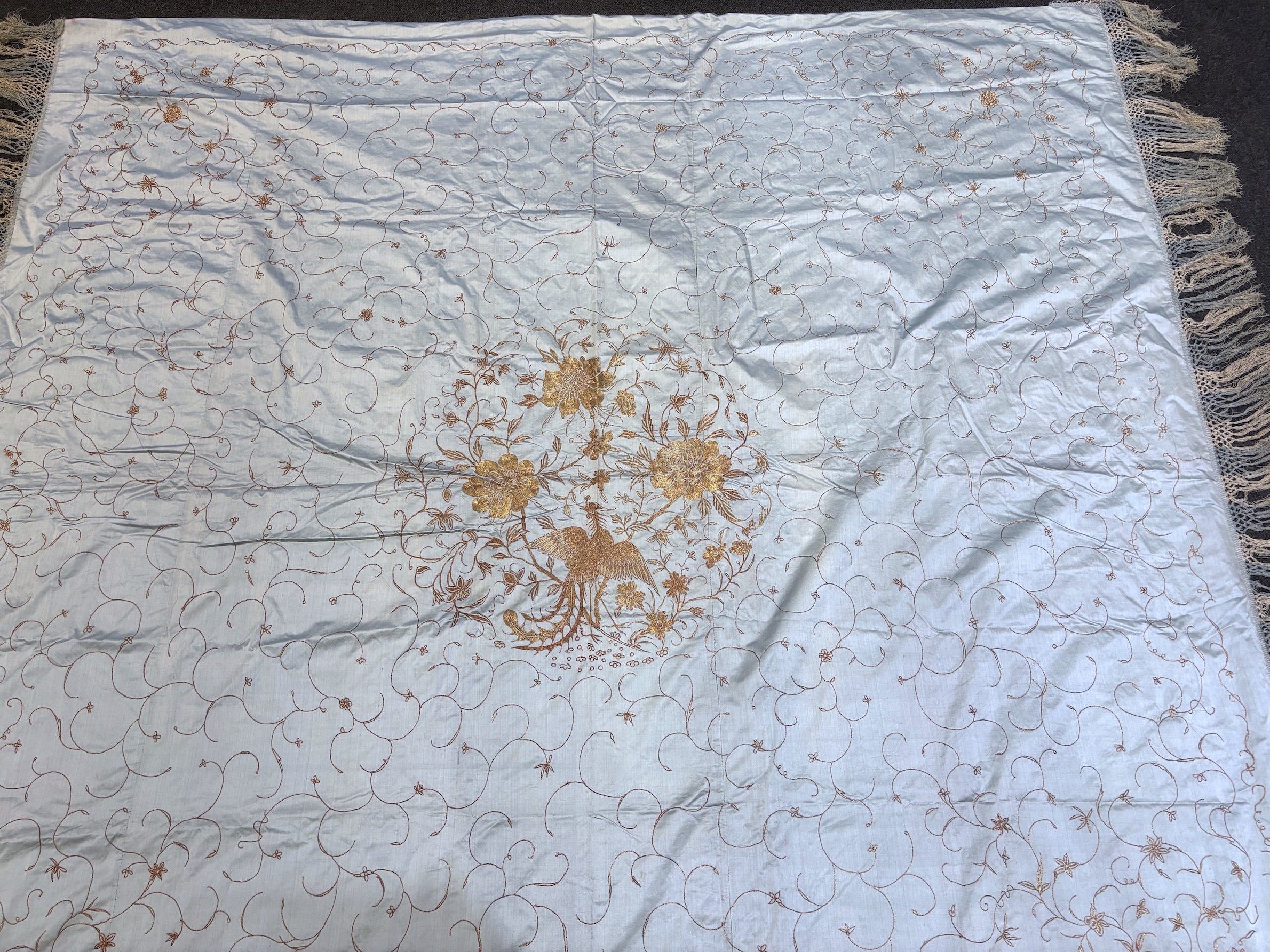 A Chinese pale grey satin silk panel edged with silk fringing, embroidered in gold with flowers and birds